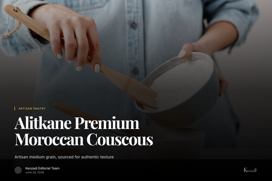 A hand sprinkling golden, fluffy Alitkane medium couscous into a traditional Moroccan ceramic bowl, with a tagine in