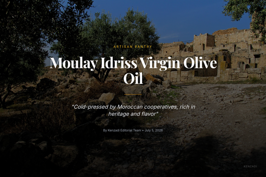 A glass bottle of golden Moulay Idriss Virgin Olive Oil on a wooden table, with a bowl of